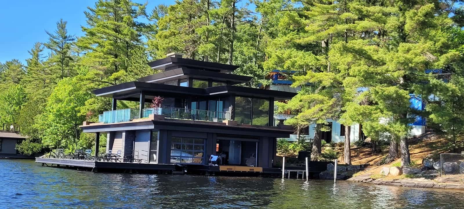 Contemporary two-storey boathouse with stacked dark roof planes, floor-to-ceiling glass and cantilevered decks in a white pine forest