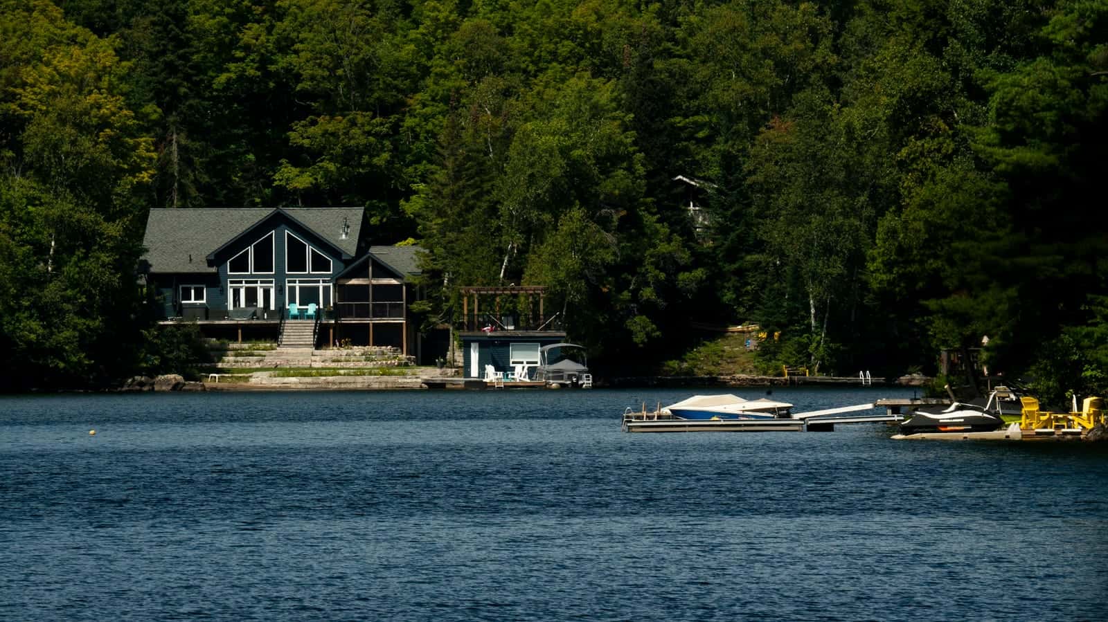 Lakeside cottage with a boathouse and docks below on a treed Canadian lake shore